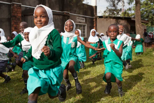 A group of children in what appears to be a warm climate dancing in green school uniforms.
