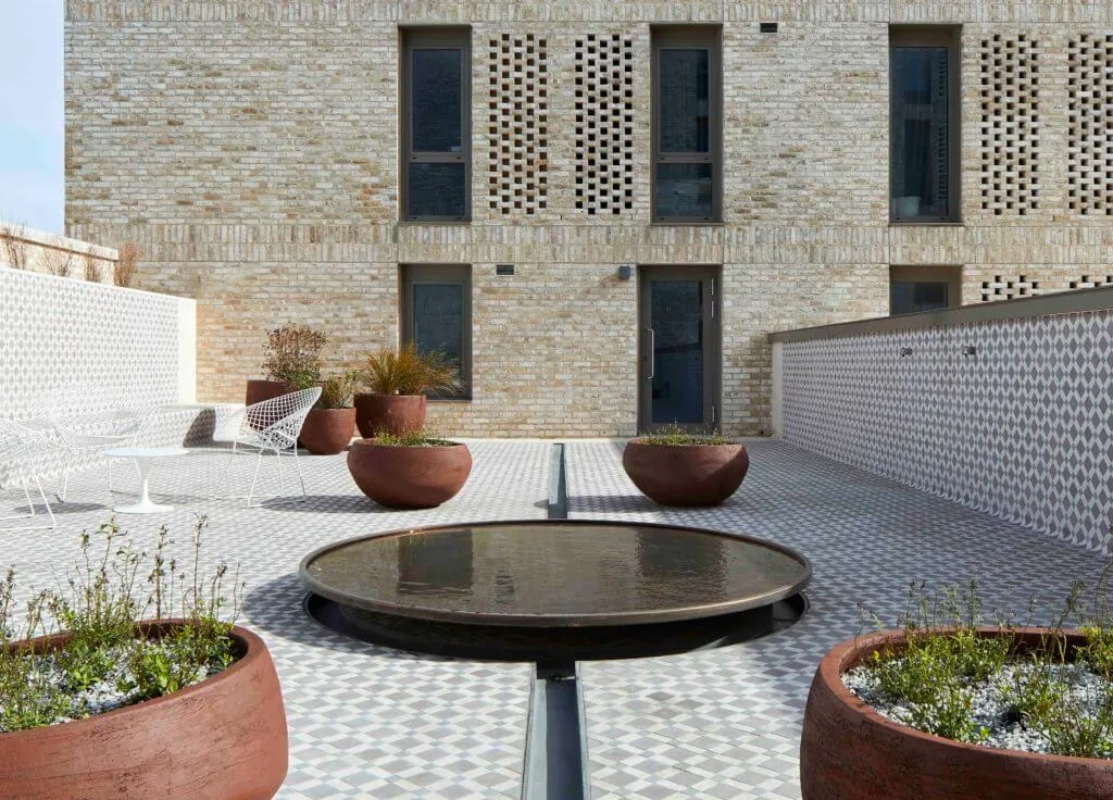 A circular pool of water with channels coming out of it, and brown round planters full of plants.