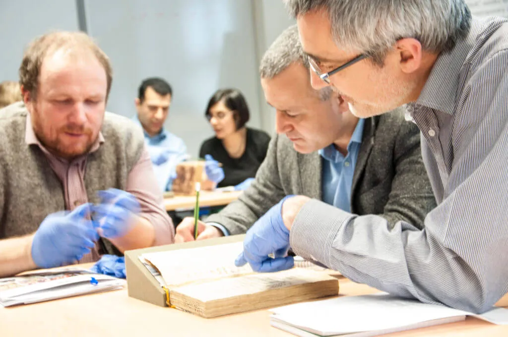 Three men looking at a text together with gloves on.